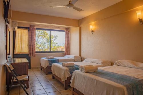 a room with three beds and a window at Hotel El Mirador in Puerto Escondido