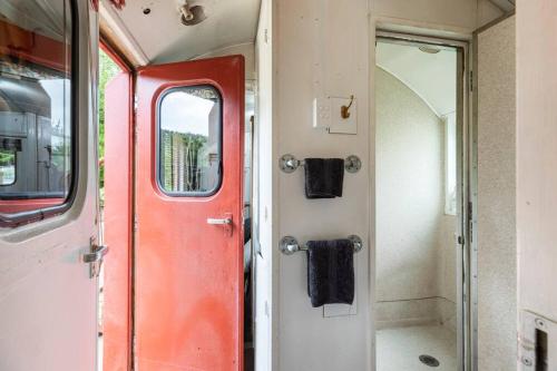 a red door of a train with two black towels at Tiny House Train-Eco stay in Upper Hutt