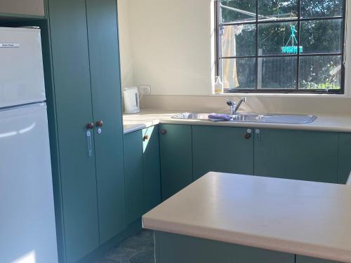 a kitchen with blue cabinets and a sink and a window at Bright Cosy Cottage in Whitianga