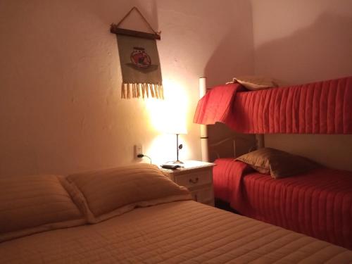 Hospedaje La Serranita في باهيا بلانكا: غرفة نوم بسريرين مع شراشف حمراء ومصباح