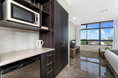 a kitchen with a microwave and a living room at Alivio Hotel Cairns in Cairns