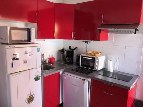 une cuisine avec des armoires rouges et un réfrigérateur blanc dans l'établissement Appartement climatisé, calme avec terrasse et parking, à 500m de la plage, 4 pers. - FR-1-607-162, au Cap d'Agde