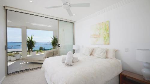 a white bedroom with a large bed and a large window at Aura 2 apartment with Spectacular Views in Shoal Bay
