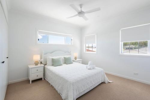 a white bedroom with a bed and two windows at Biirinba Top Floor - oceanstays in Yamba