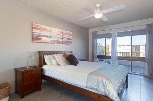 a bedroom with a bed with a ceiling fan and a window at The Dunes Two bedroom apartment overlooking pool in Fingal Bay