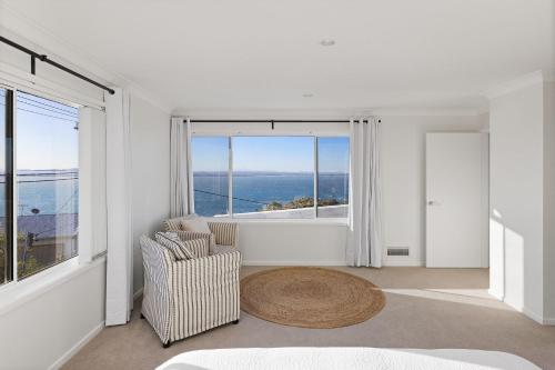 Cette chambre blanche dispose d'une chaise et d'une grande fenêtre. dans l'établissement Tranquil with Harbour Views, à Nelson Bay