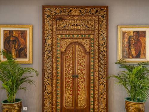 une porte en bois ornée dans une pièce avec deux plantes dans l'établissement Tirtha Bayu Estate by Elite Havens, à Tanah Lot