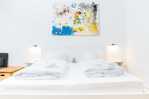 two white beds in a room with a painting on the wall at HEIMATEL - Suiten, Apartments und Studios in Scheidegg