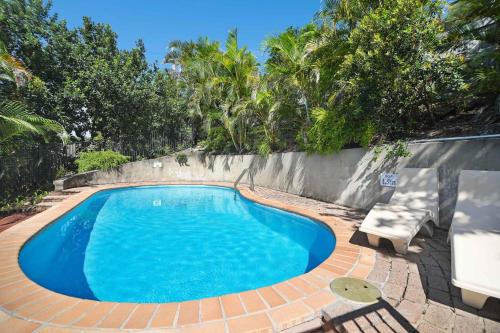 a blue swimming pool with a brick wall and trees at Kari in Peregian Beach in Peregian Beach