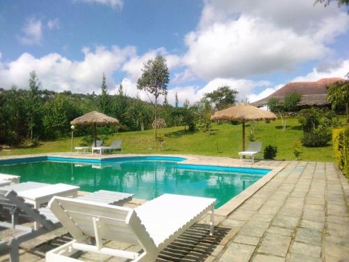 a swimming pool with white chairs and umbrellas at Andasibe Sifaka Lodge in Andasibe