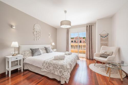 a white bedroom with a bed and a chair and a window at Villa Alma Azul in Llucmajor
