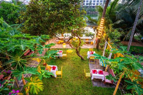 a patio with tables and chairs in a garden at Hoi An Green Riverside Oasis Villa in Hoi An