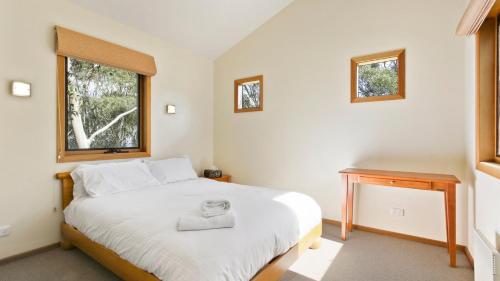 a bedroom with a bed and a desk and two windows at Jasandre in Dinner Plain