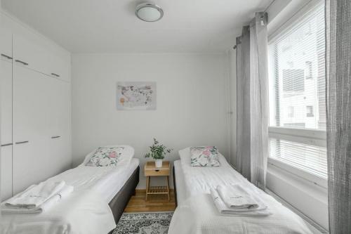 two beds in a white room with a window at Kotimaailma Joensuu - Saunallinen kolmio keskustassa in Joensuu