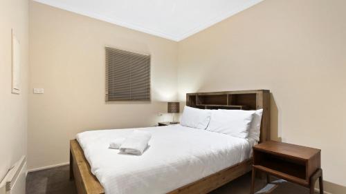 1 dormitorio con 1 cama blanca grande y cabecero de madera en Prosecco en Dinner Plain