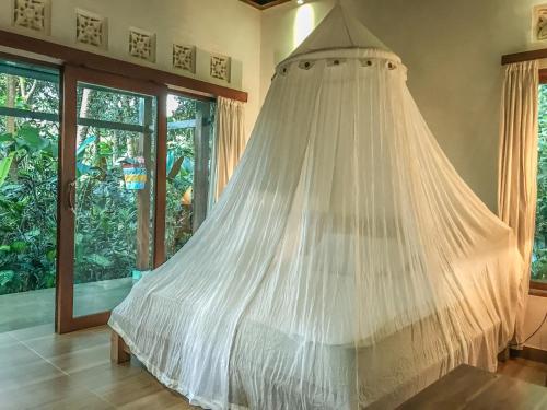un letto con zanzariera in una camera con finestre di Cozy Wayan Sueta's Garden Villa 2 ad Ubud