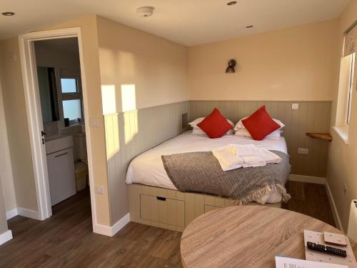 Un dormitorio con una cama con almohadas rojas y una mesa. en MAESLLAN CABINS 'Hud Y Machlud', en Cross Inn
