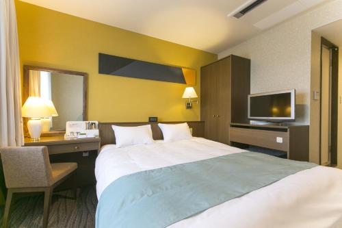 a hotel room with a bed and a desk and a tv at Fujisan Station Hotel in Fujiyoshida