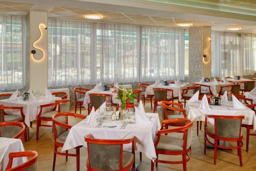 a restaurant with white tables and chairs and windows at Augusta SPA Hotel in Hisarya