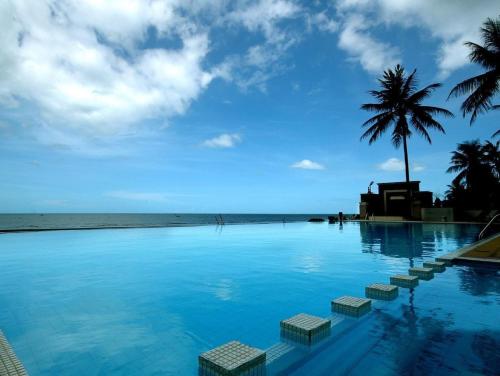 una piscina con una palma e l'oceano di Golden Pine Beach Resort a Pran Buri