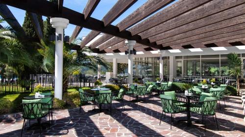 a patio with green tables and chairs under a wooden ceiling at Amadria Park Beach Hotel Niko in Šibenik