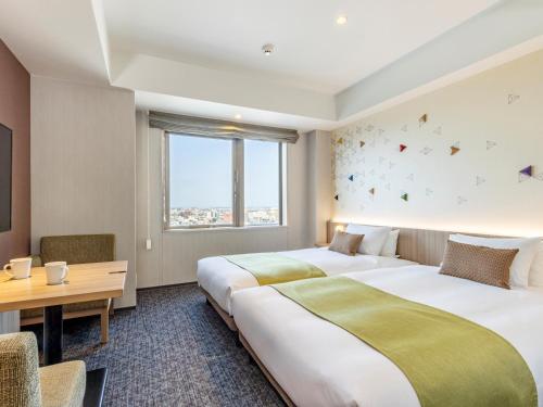 Cette chambre comprend deux lits, un bureau et une table. dans l'établissement Tokyu Stay Kanazawa, à Kanazawa