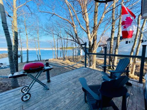 a deck with chairs and a grill and a flag at Lucky Bay Hideaway - Seaview Sauna & cedar hot tub in Campbellton