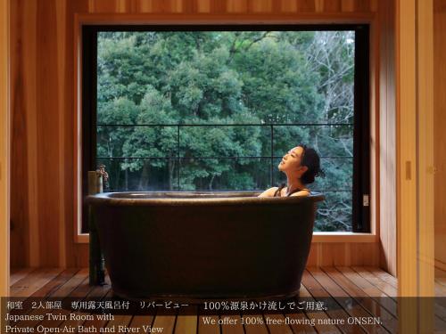 a woman sitting in a bath tub in front of a window at Tatsuta Ryokan in Izu