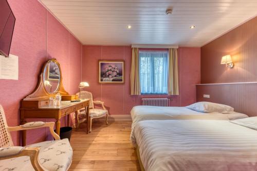 聖胡伯特的住宿－Hôtel Le Cor de Chasse，酒店客房设有两张床、一张桌子和一面镜子