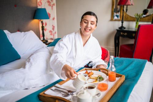 a woman sitting on a bed with a tray of food at The Roseate Villa Bath in Bath