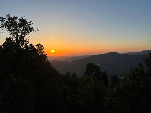 a sunset in the mountains with trees in the foreground at Ortus - Murree Hills in Murree