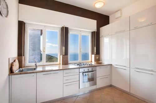 a kitchen with white cabinets and a large window at Villetta Olivi - Vista mozzafiato in Torri del Benaco