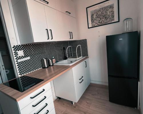 eine Küche mit weißen Schränken und einem schwarzen Kühlschrank in der Unterkunft Studio Lumineux- à 15 min de Paris in Bois-Colombes