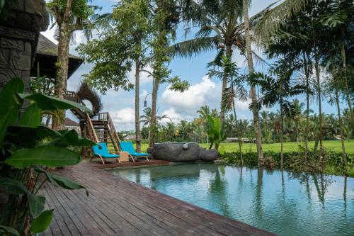 a pool at a resort with chairs and palm trees at Uma Linggah Resort in Tampaksiring