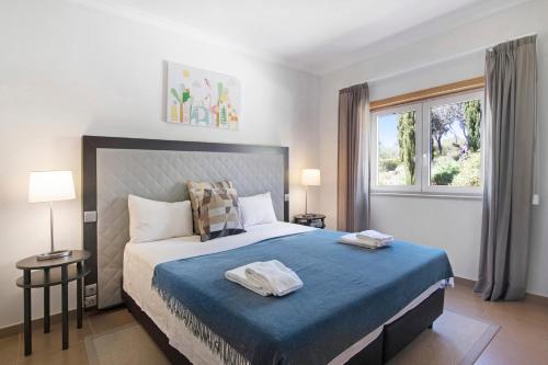 um quarto com uma cama com lençóis azuis e uma janela em V2 Vale da Ribeira em Mexilhoeira Grande