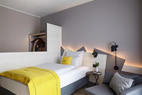 1 dormitorio con 1 cama con manta amarilla y silla en acora Düsseldorf Airport Living the City - Apartments en Düsseldorf