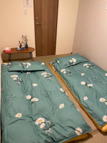 two beds in a room with green comforter with flowers at W&J Dream Stay in Osaka