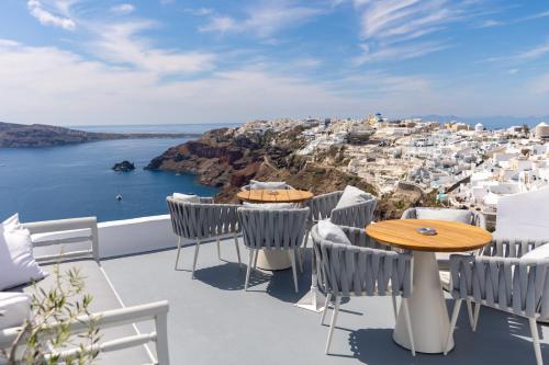 a balcony with tables and chairs and a view of a city at IKIES Santorini in Oia