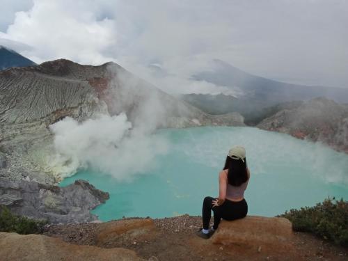 a woman sitting on the edge of a cliff overlooking a blue lake at Ijen Farmer Homestay in Banyuwangi