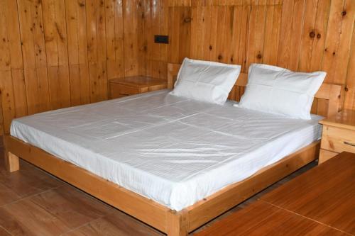 a bed with white sheets and pillows in a wooden room at Hotel Royal Hillcrest in Harsil