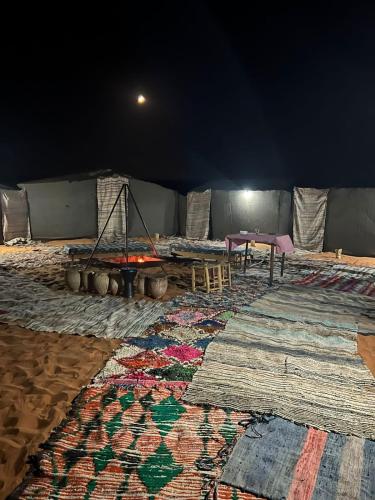 a room with a table and a large rug at Merzouga Camp and Hostel in Merzouga