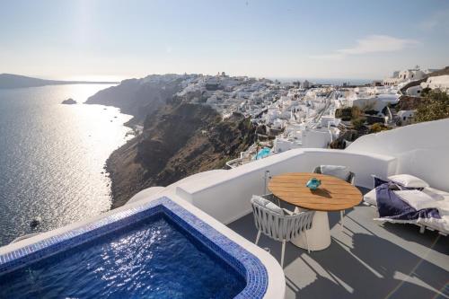a balcony with a pool and a table and the ocean at IKIES Santorini in Oia