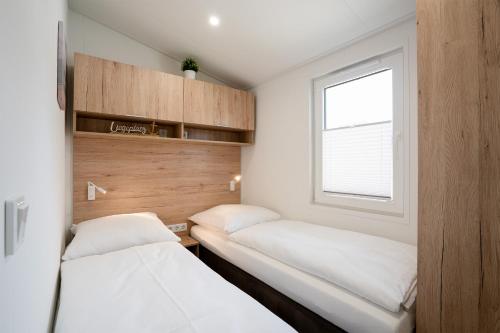 two beds in a small room with a window at Ostseecamp Ferienhaus "StrandPerle" in Scharbeutz