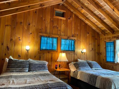 two beds in a room with wooden walls and windows at Amber Lantern Duplex Cottage in Lake George
