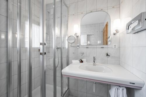 a white bathroom with a sink and a shower at Hotel Nevada in Samnaun