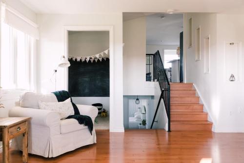 a living room with a white chair and a staircase at Fox Lane - Prince Edward County Farmhouse in Picton