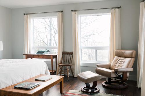 a bedroom with a bed and a chair and two windows at Tanglewood - Large Waterfront Home in PEC in Waupoos