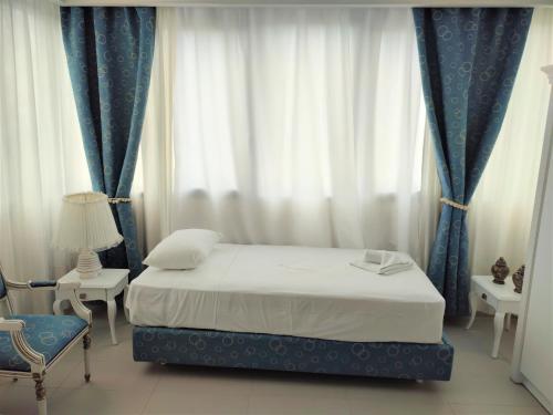 a bedroom with a bed and blue curtains and a chair at Light Blue Hotel in Nea Kalikratia