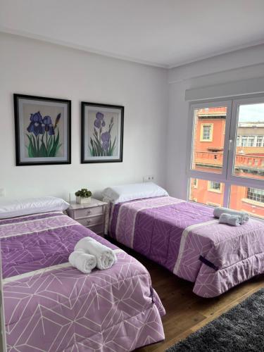 two beds in a room with purple sheets and a window at Tía Ana in Gijón
