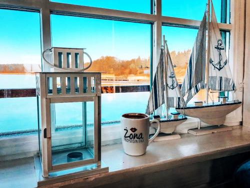 a table with a coffee cup and a toy sailboat in a window at Piękny Dom na wodzie!!! Mazury szlak WJM in Ryn